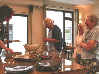 2 UK older women laughing Maura serving food | Retreat venue